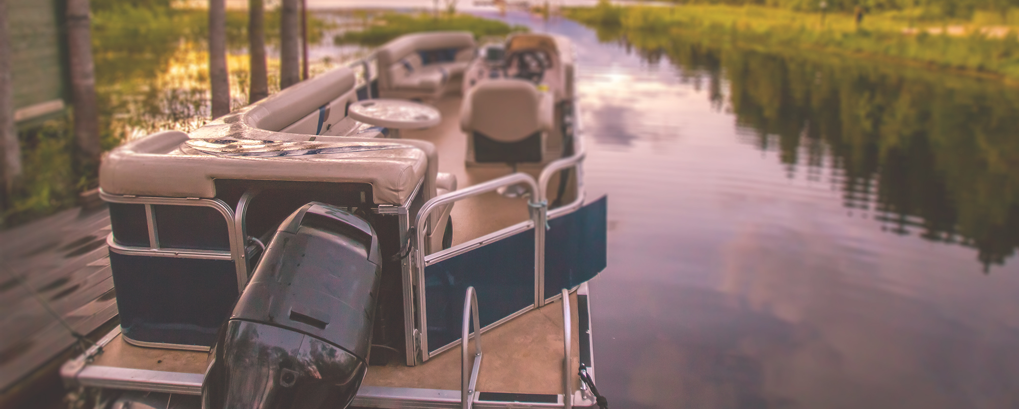 Large pontoon boat with black outboard motor sitting on a river along the shore